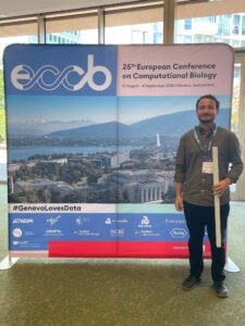 Carlos Cruz junto al banner de su investigación en el Conferencia Europea de Biología Computacional en Ginebra, Suiza.
